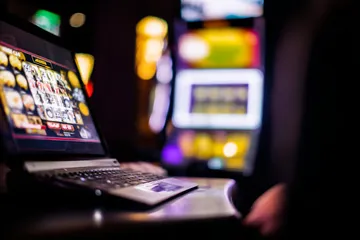 A woman smiling by bright slot machines showing lucky symbols, showcasing the exciting slot offerings at 1XBED.
